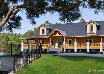 Modern log home with wraparound porch and trees.