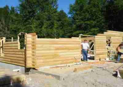 Workers constructing a log cabin structure outdoors.