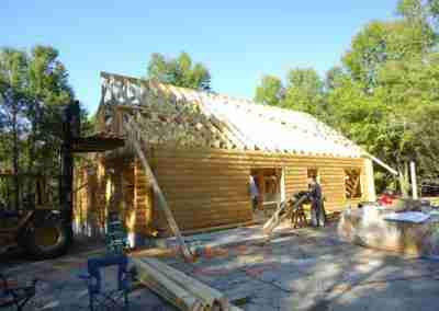 Log cabin under construction in a wooded area.