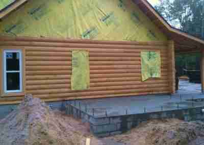 Log cabin under construction with yellow insulation.